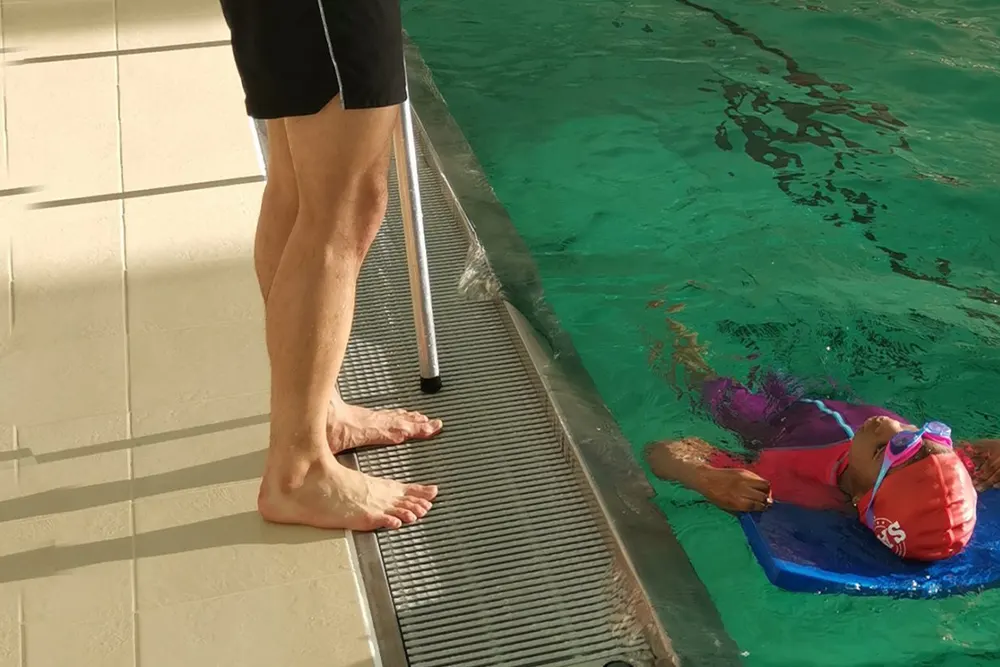 An instructor guiding a young swimmer from the poolside.
